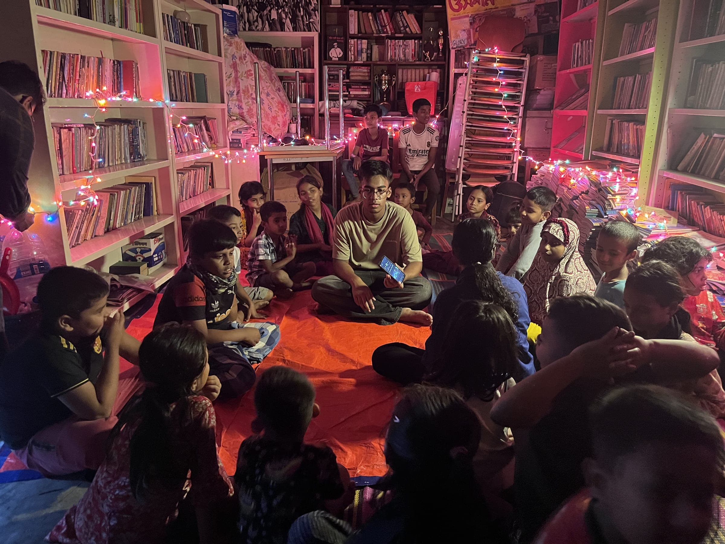 Children sitting together on the floor of a library decorated with festive lights