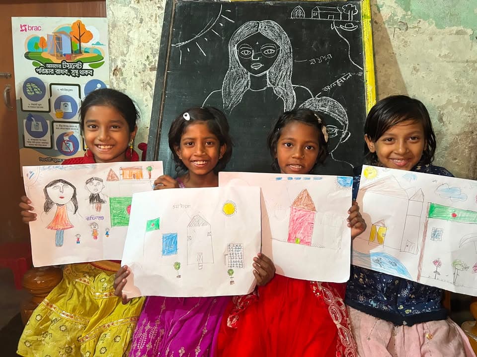 Four girls in bright dresses holding up their drawings in front of a chalkboard